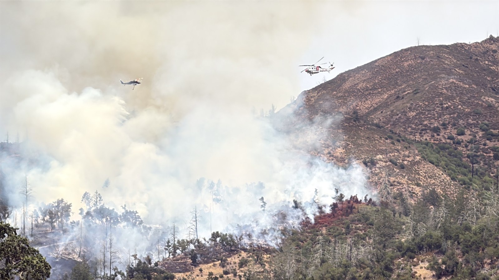 Helicopters work the ridge through the smoke.